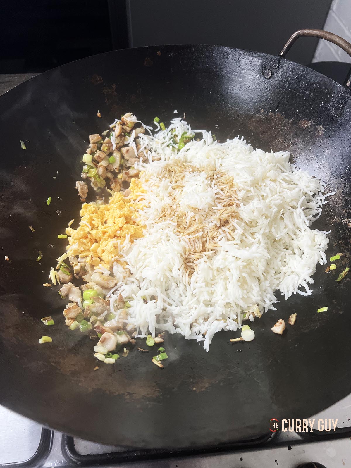 Adding the scrambled eggs and cold rice with sesame oil to the wok.