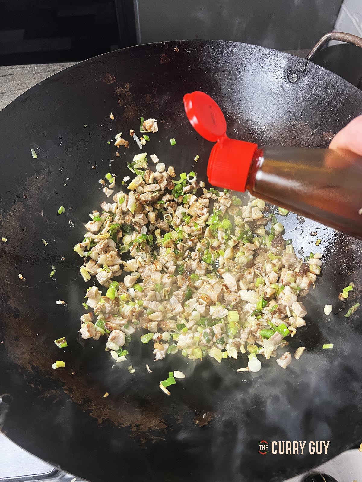 Adding soy sauce to the ingredients in the wok.