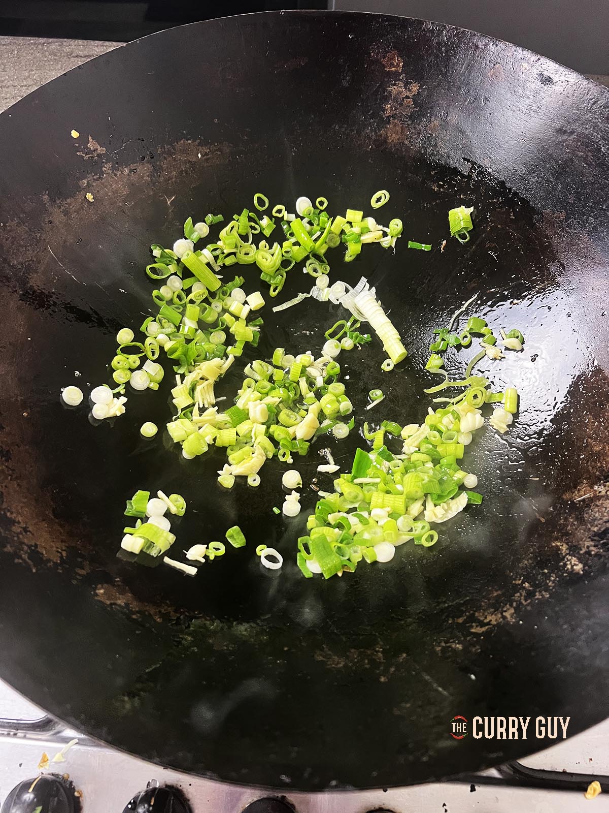 Frying spring onions (scallions), garlic and ginger in a wok.