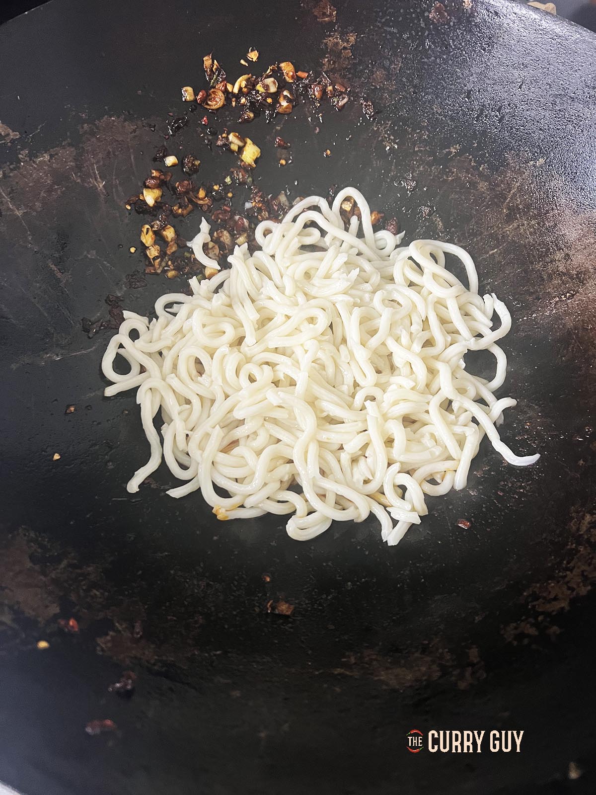 Adding cooked noodles to the wok.