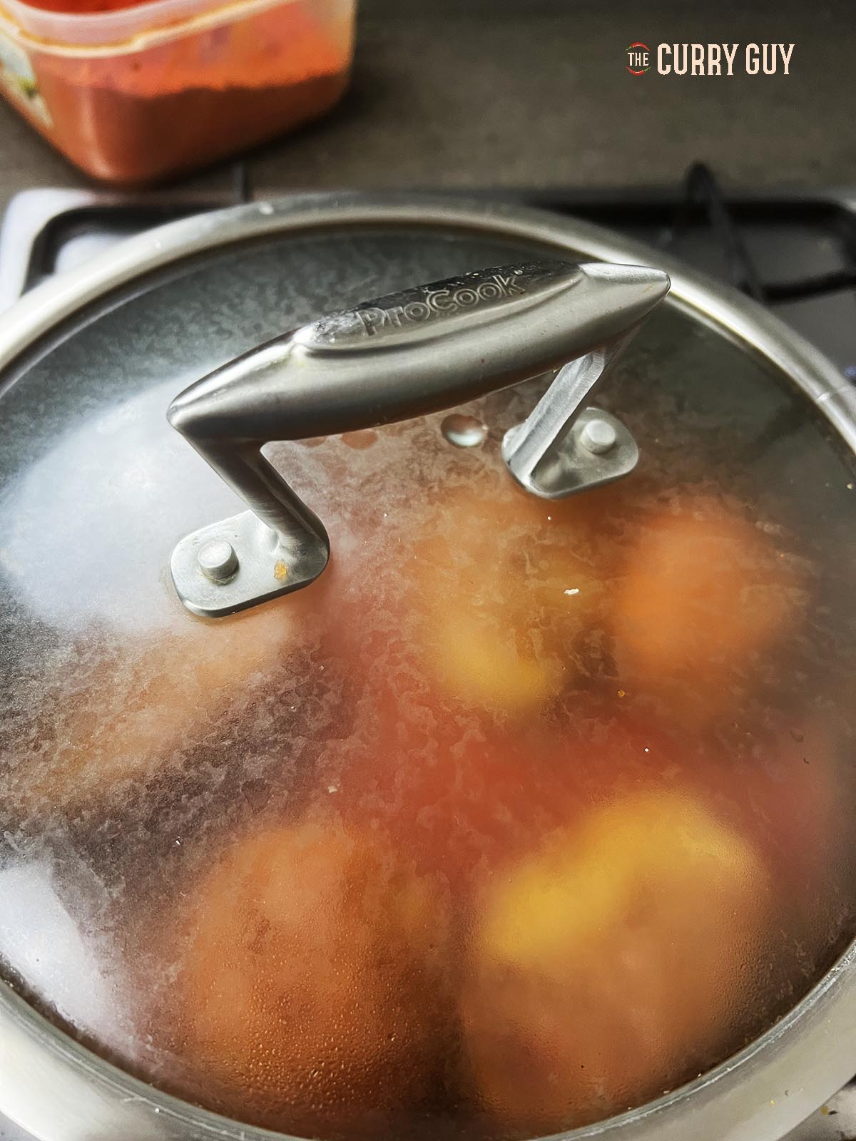 Potatoes cooking in the curry sauce in a covered pan.