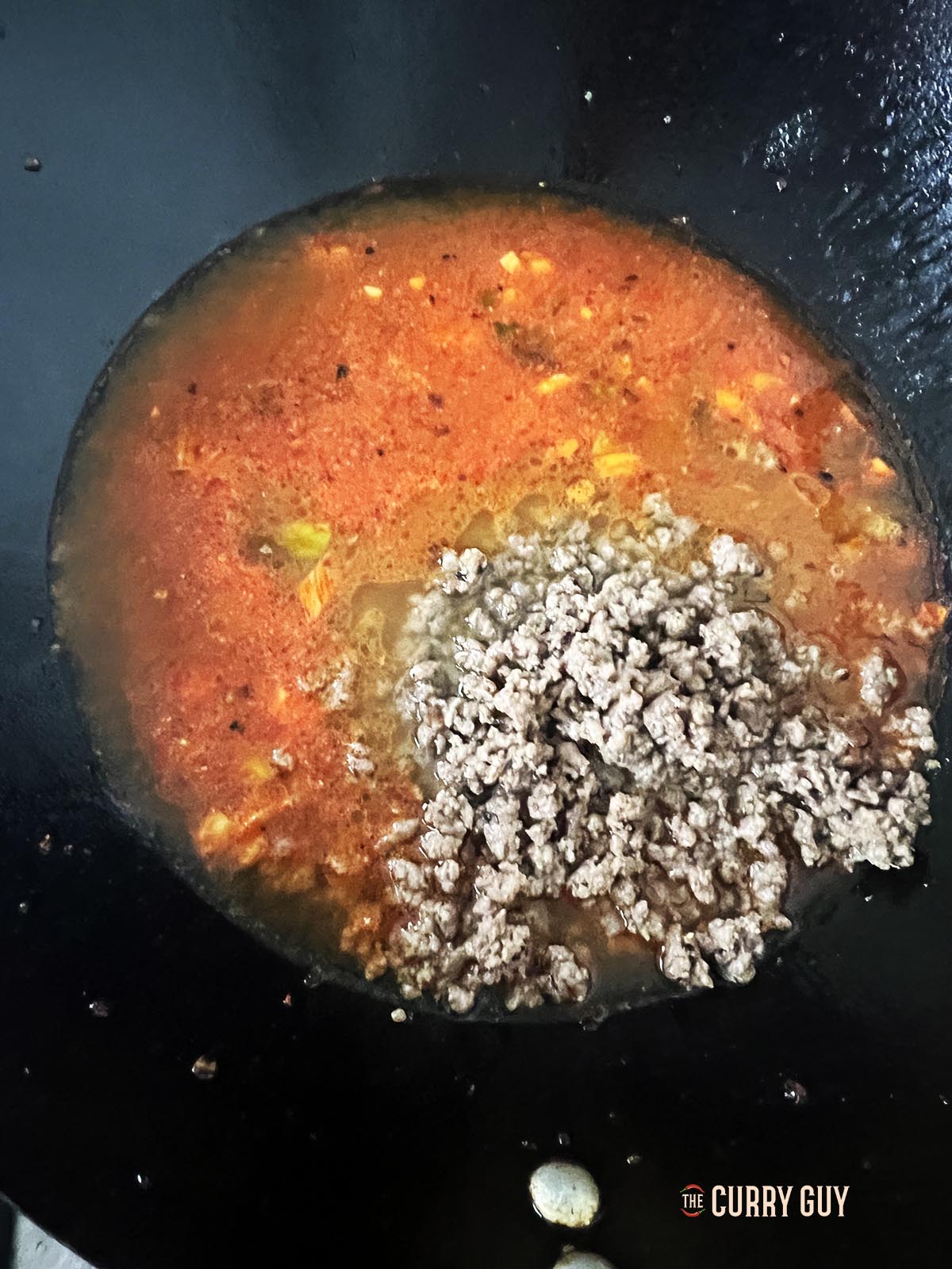 Adding the stock and half of the cooked minced meat to the wok.