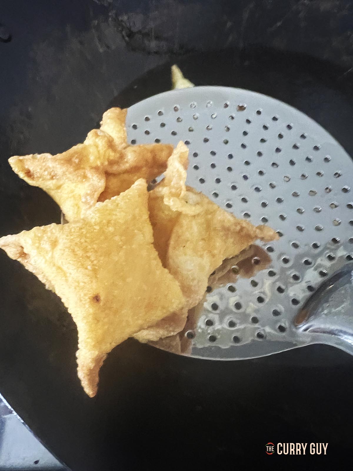 Transferring the cooked rangoon parcels to a wire rack to drain any excess oil.