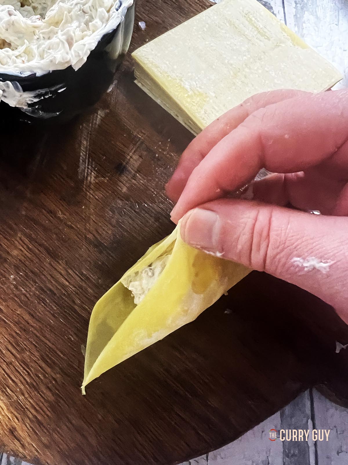 Bringing two opposite corners of the wonton wrapper together and pressing them together.