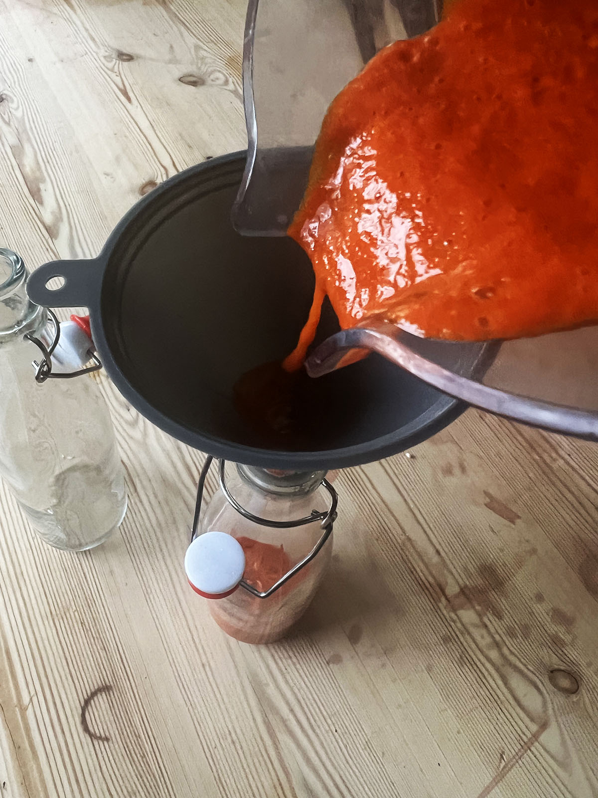 Pouring the sriracha sauce through a funnel into a bottle.