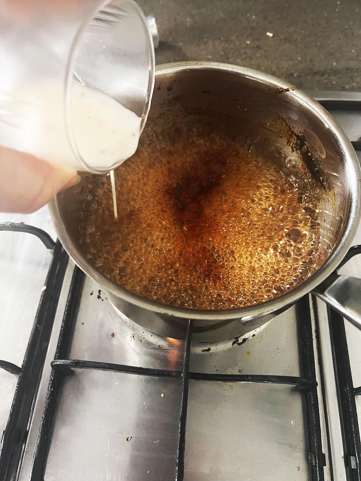 Adding the slurry to thicken the sauce and also food colouring.