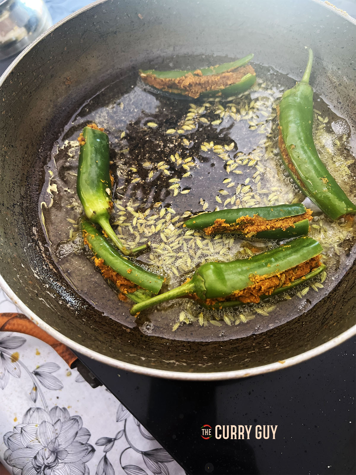 Heating oil and tempering the fennel and cumin seeds. Then adding the stuffed chillies.