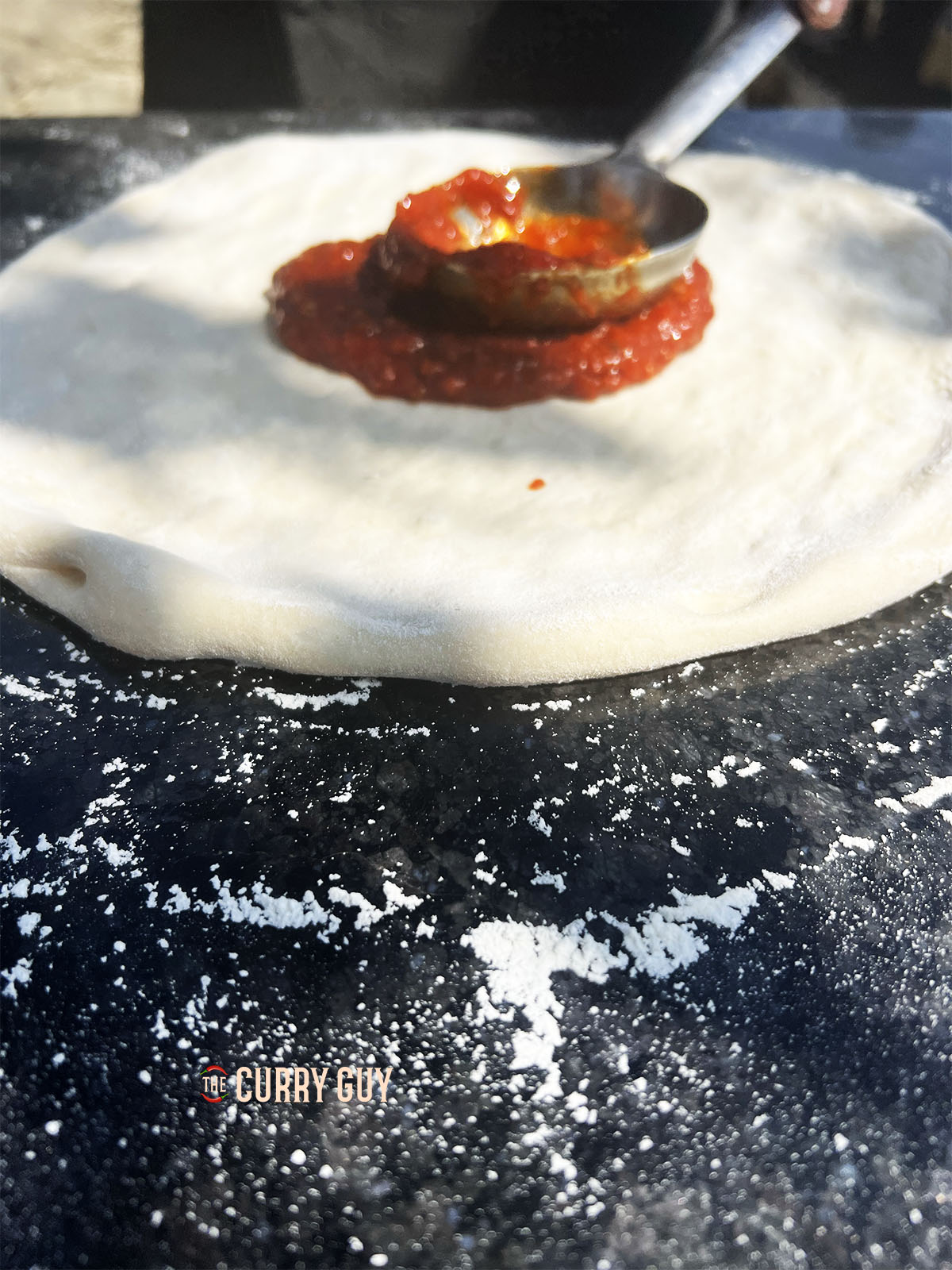 Covering the naan pizza base with tomato sauce.
