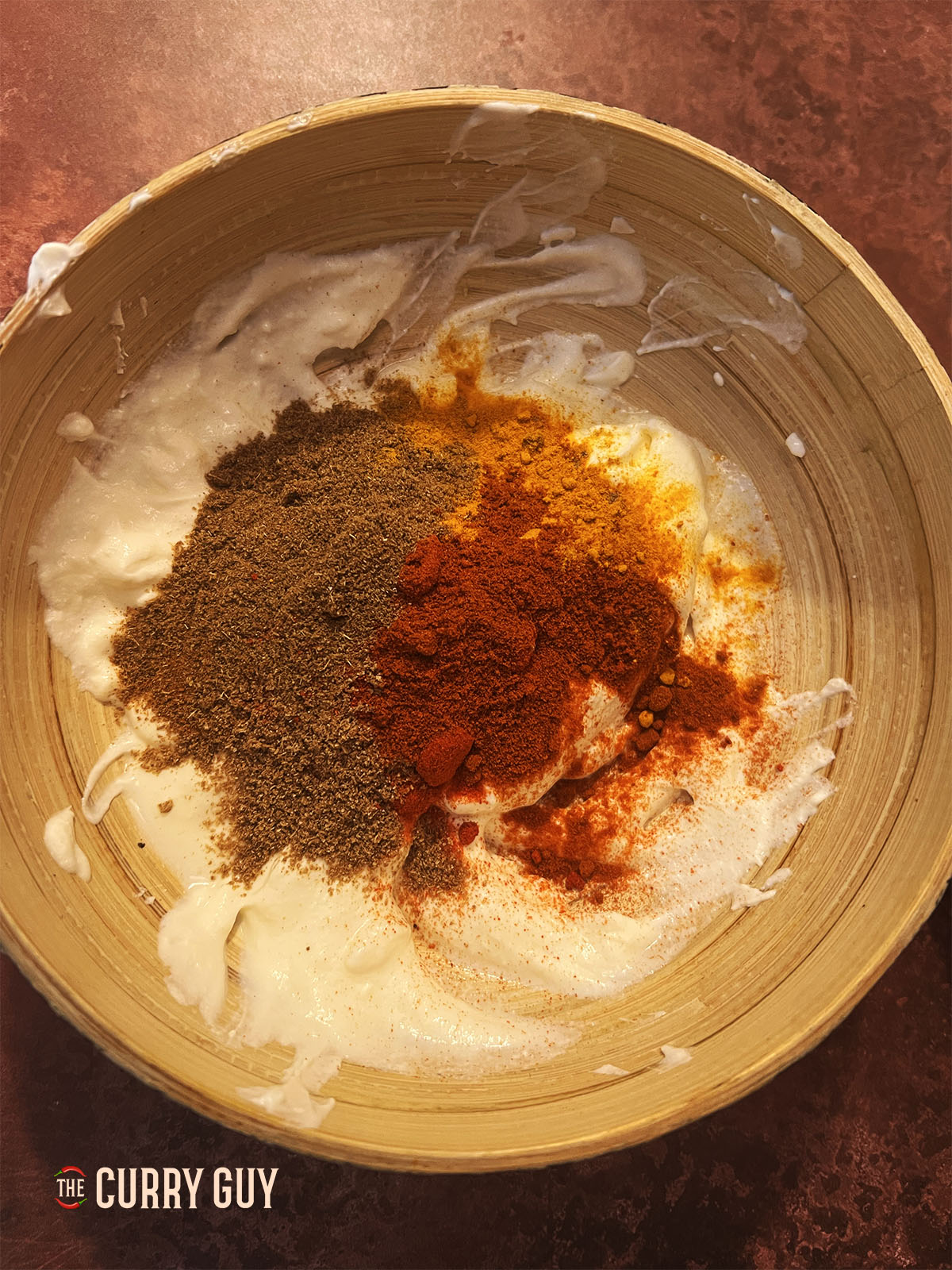 Adding the garlic and ginger paste and the spices to the yoghurt base.