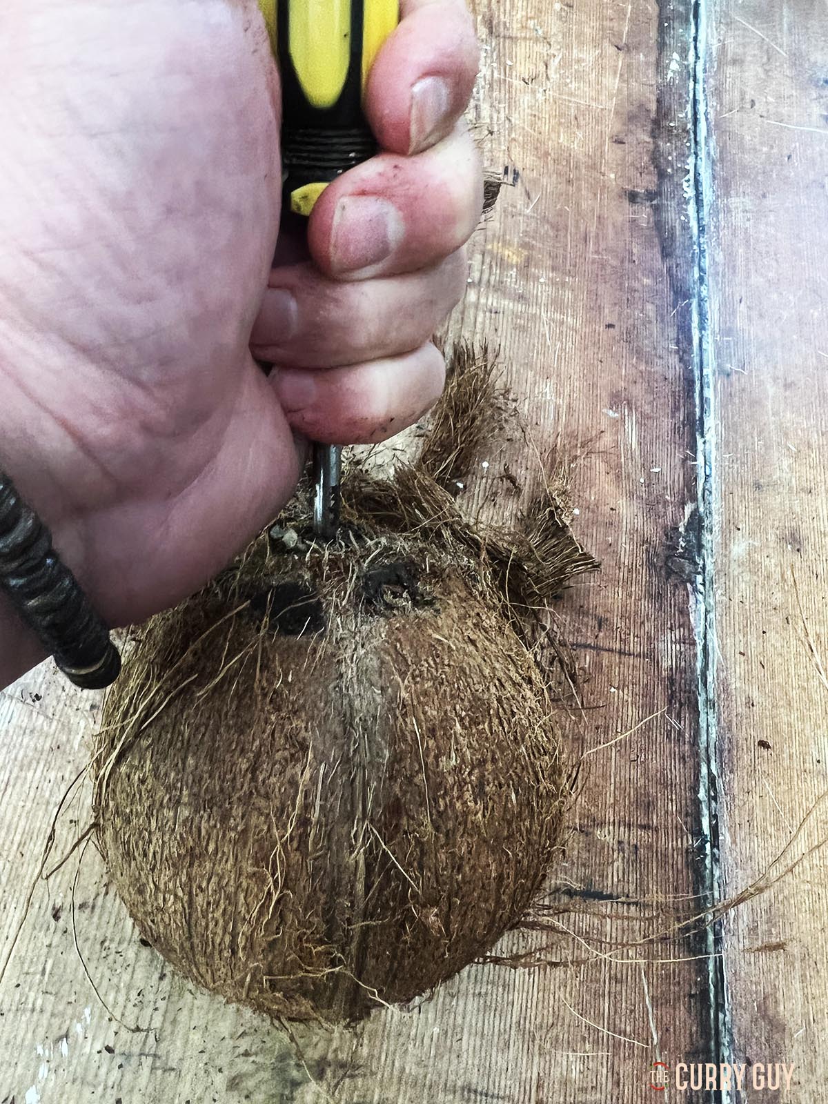 Pushing a screwdriver through one of the eyes of the coconut.