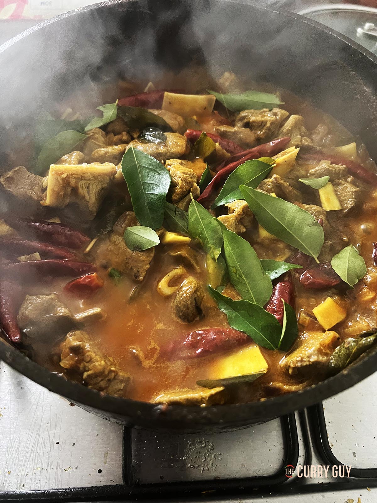 Adding the cooked meat and reduced stock to the curry pan.