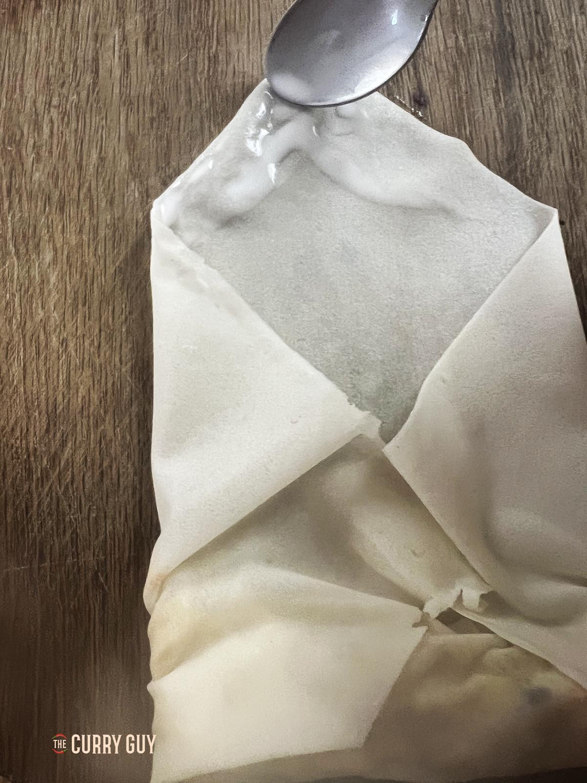 Linking the top corner of the wrapper with a flour and water mixture to seal the spring roll shut.