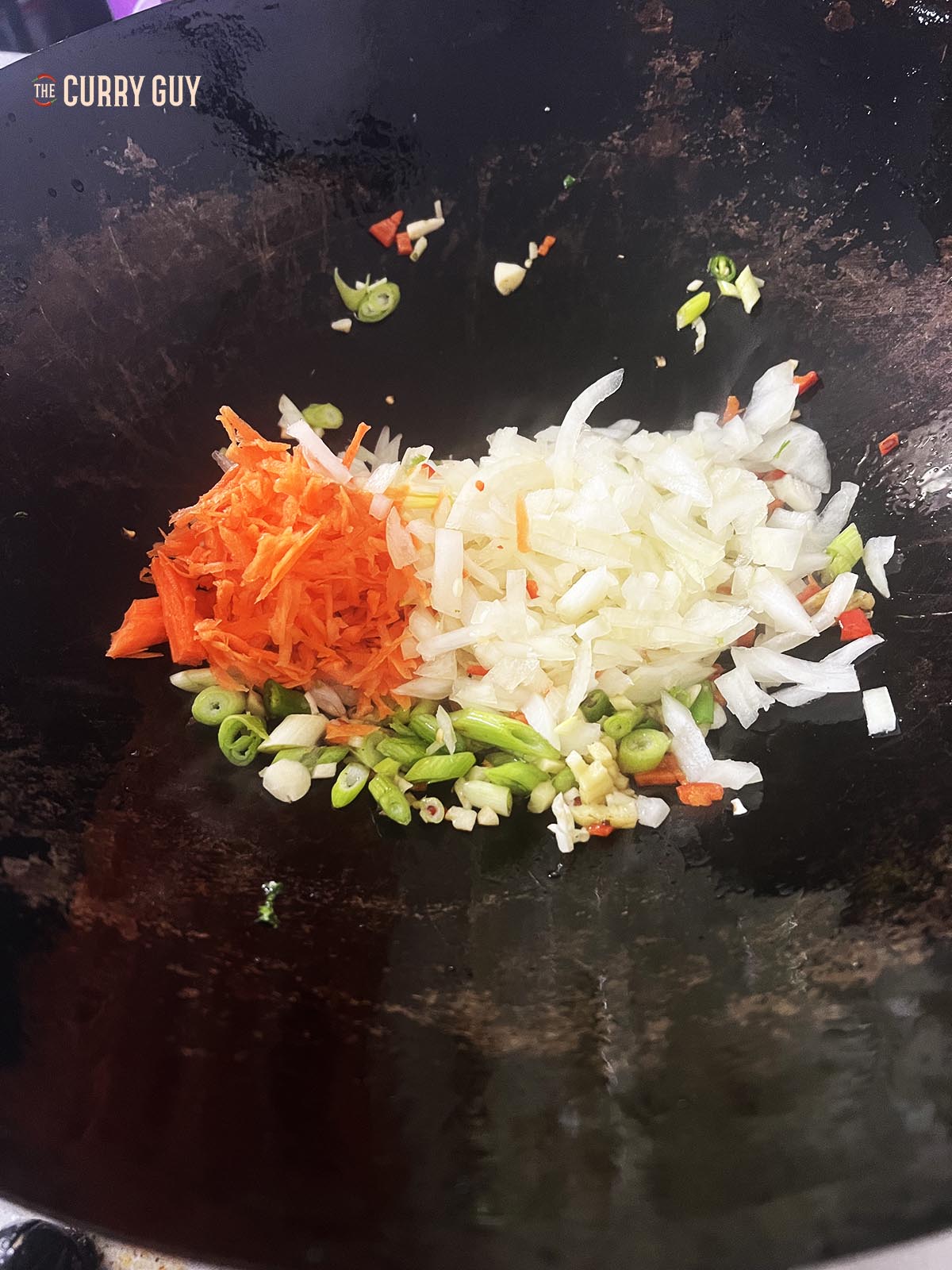 Adding the grated carrot and chopped onion to the wok.