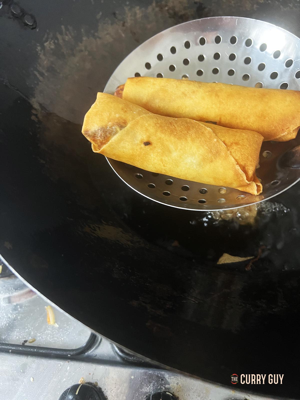 Transferring the fried spring rolls to a paper towel to drip the excess oil.