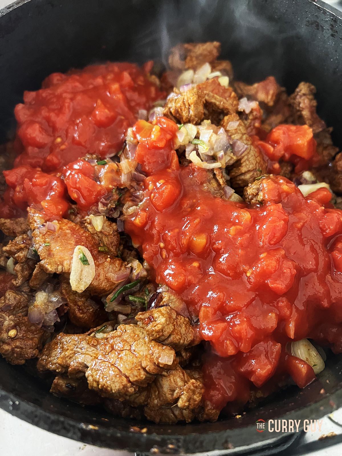 Returning the seared beef to the pan and adding chopped tomatoes.