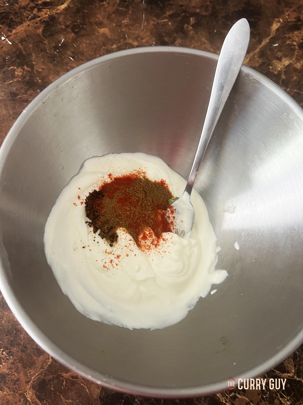 Adding the ground spices to the whisked yoghurt.