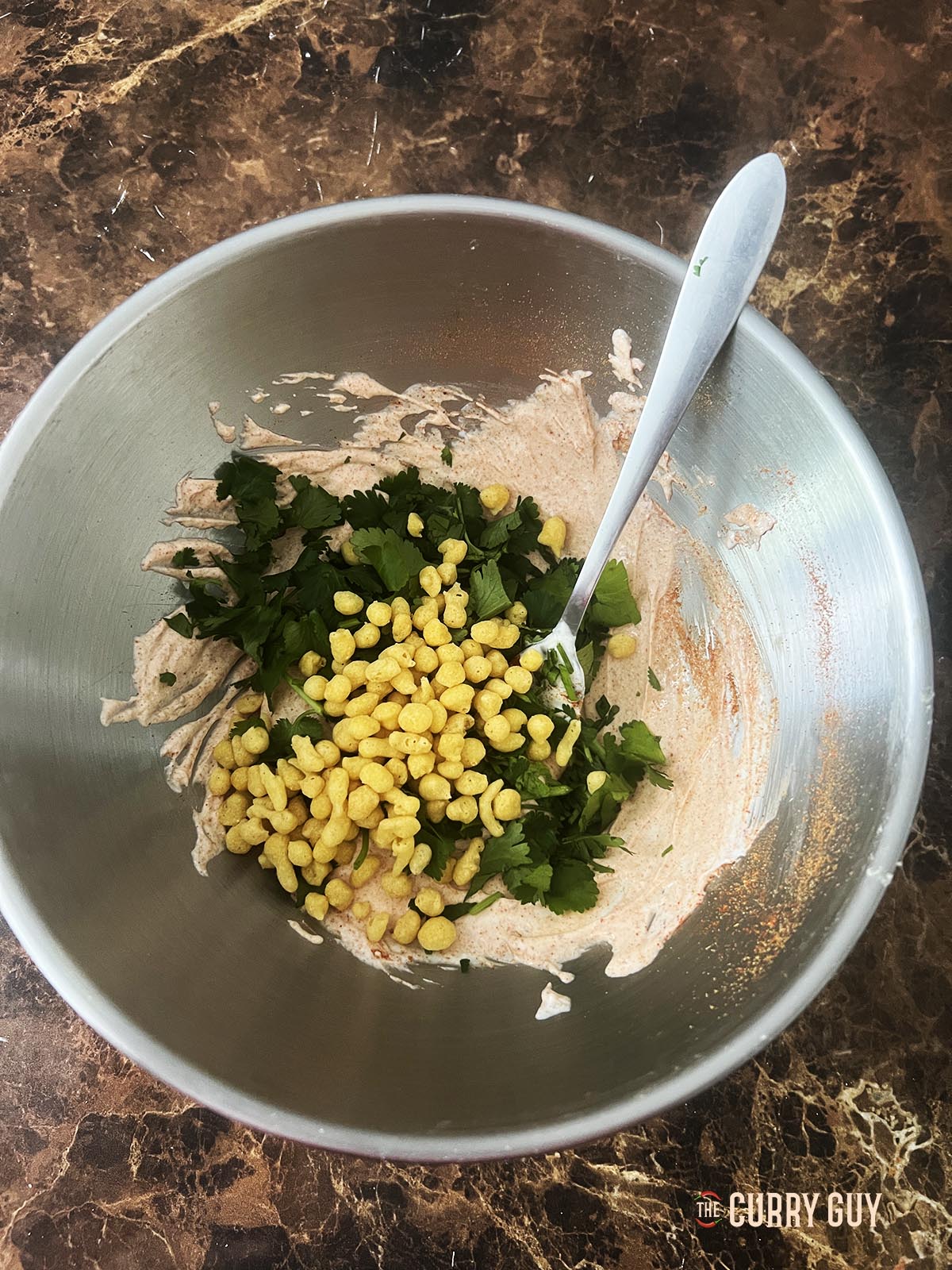 Adding a couple of tablespoons of boondi and coriander (cilantro) to the yoghurt and spices.