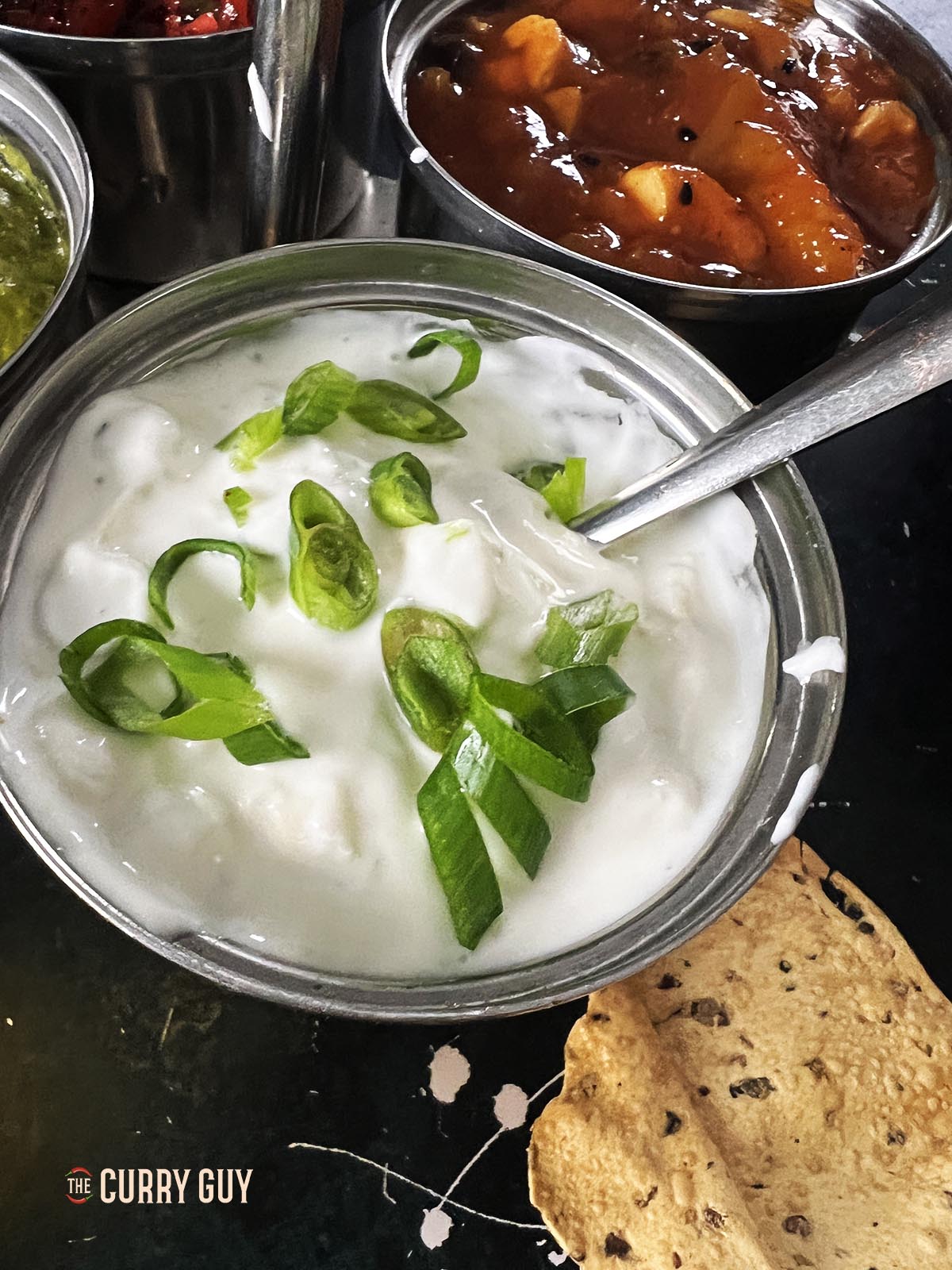 Onion raita in a serving dish, garnished with more spring onion.