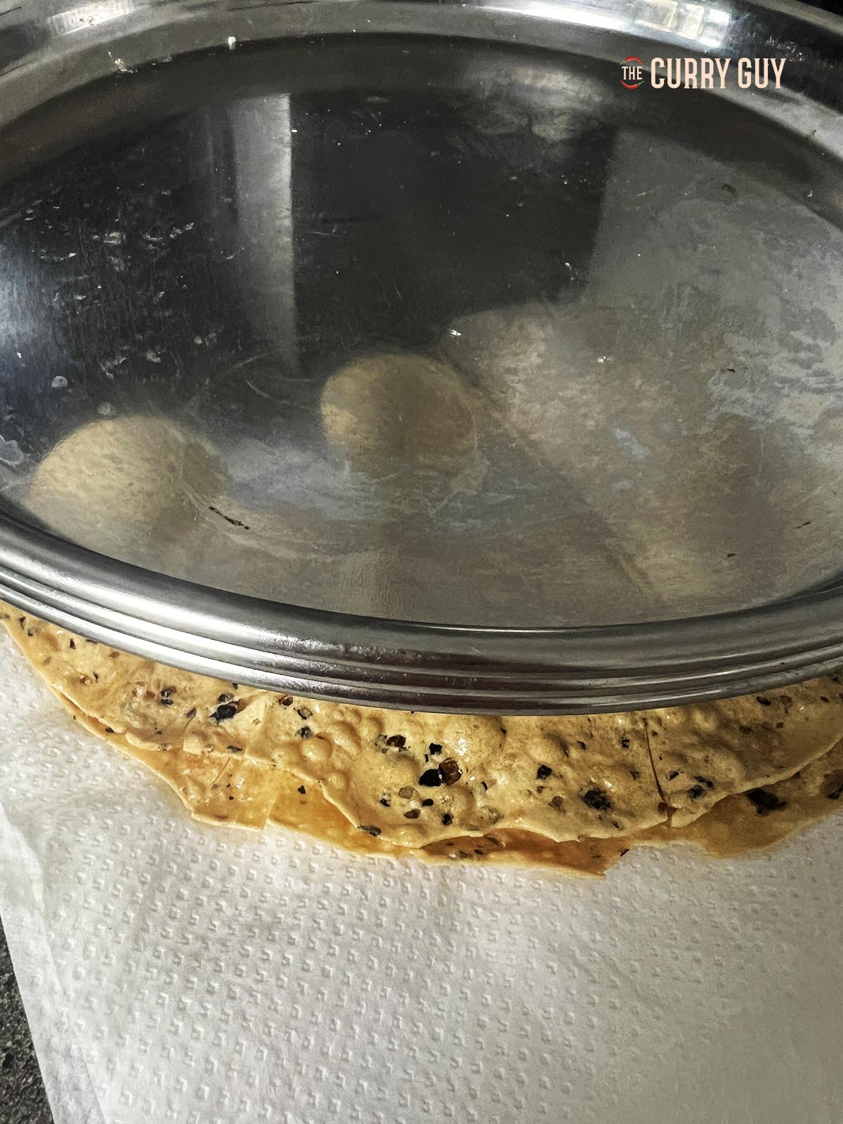 Placing a plate on top of two freshly fried poppadoms to weight them down and make them flat.