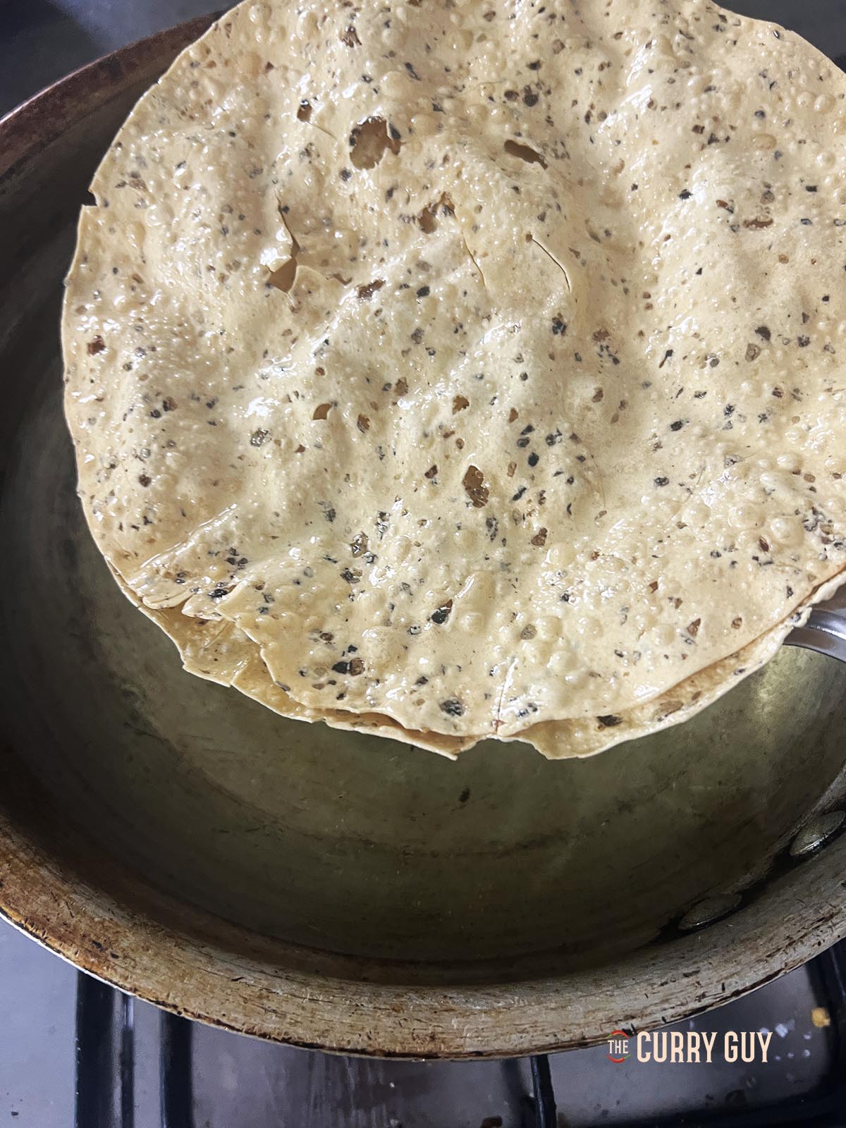 Two cooked poppadoms being coming out of the oil using tongs.