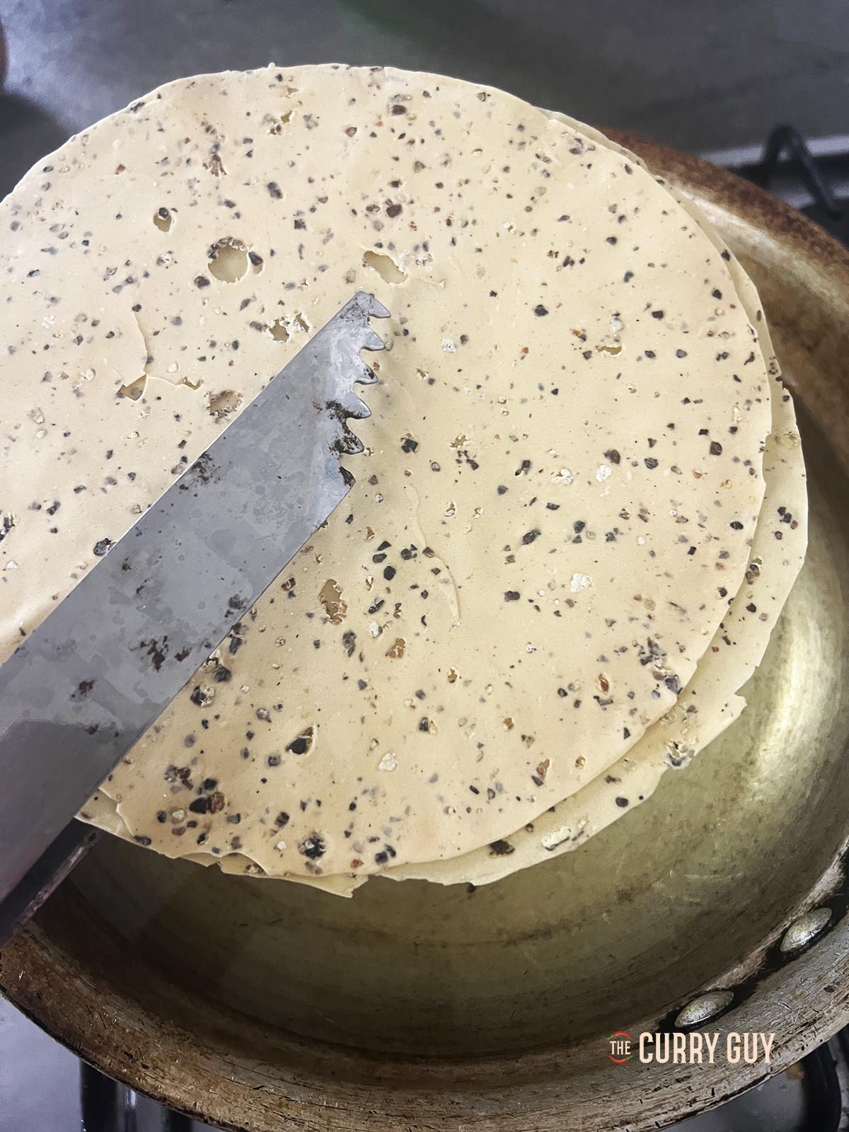 Using tongs to place two papads in hot oil to fry into poppadoms.