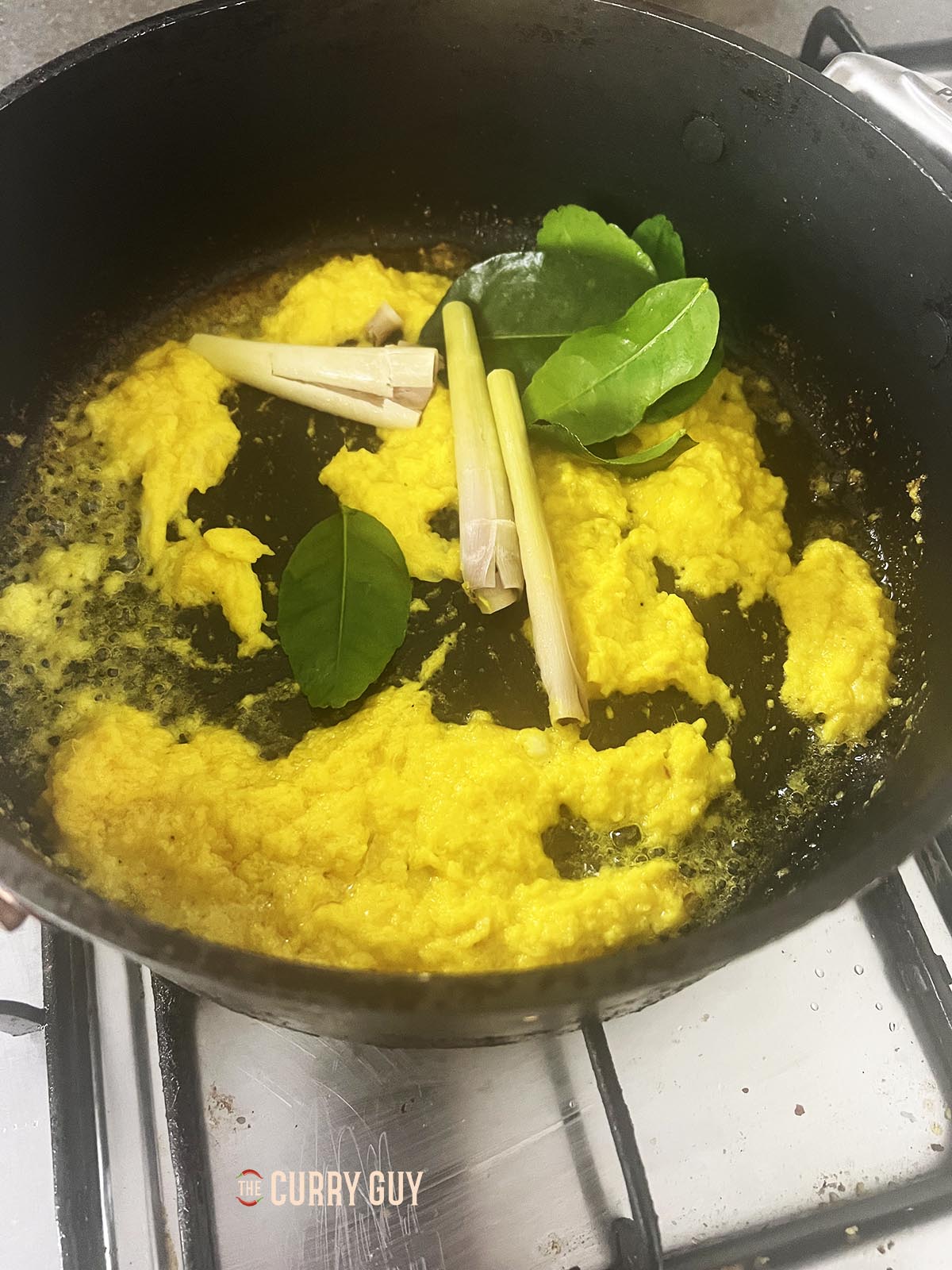 Adding the lemongrass and makrut lime leaves to the paste in the pan.