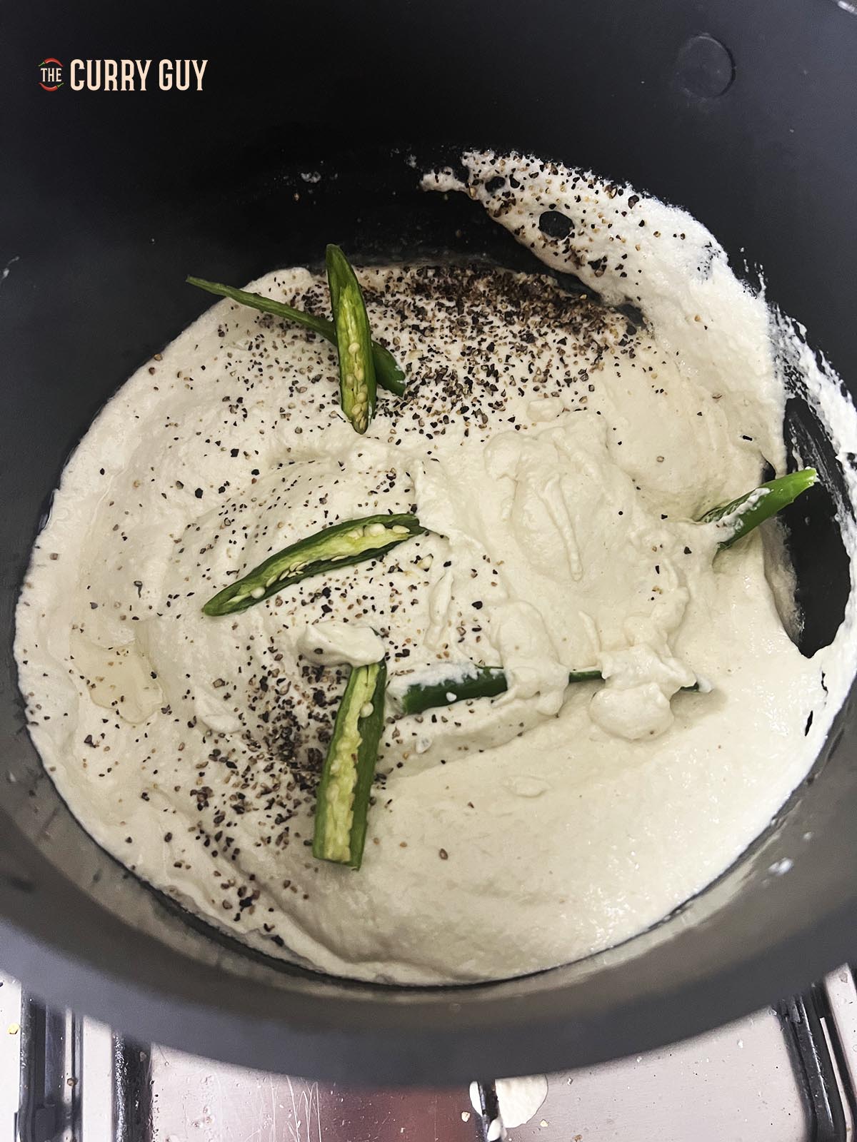 Adding green chillies, salt and white pepper to the simmering sauce.
