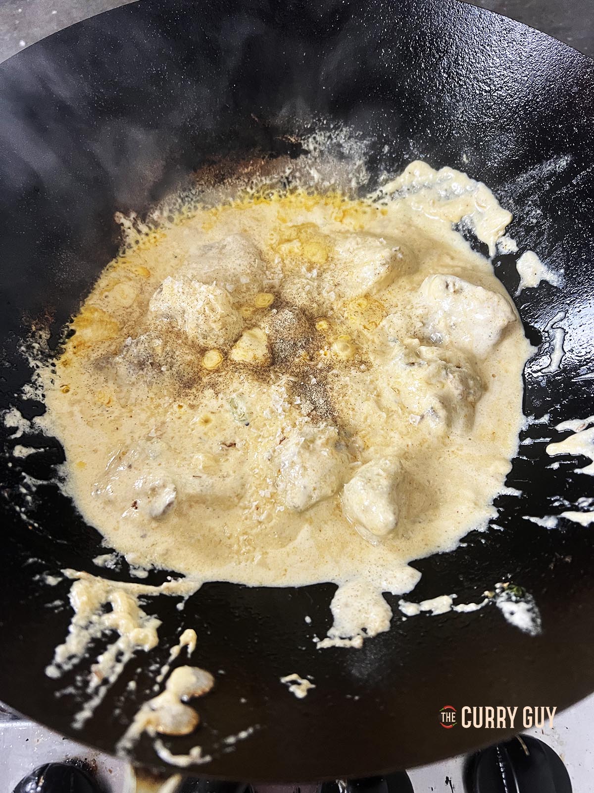 Adding ground turmeric and white pepper to the sauce in the wok.