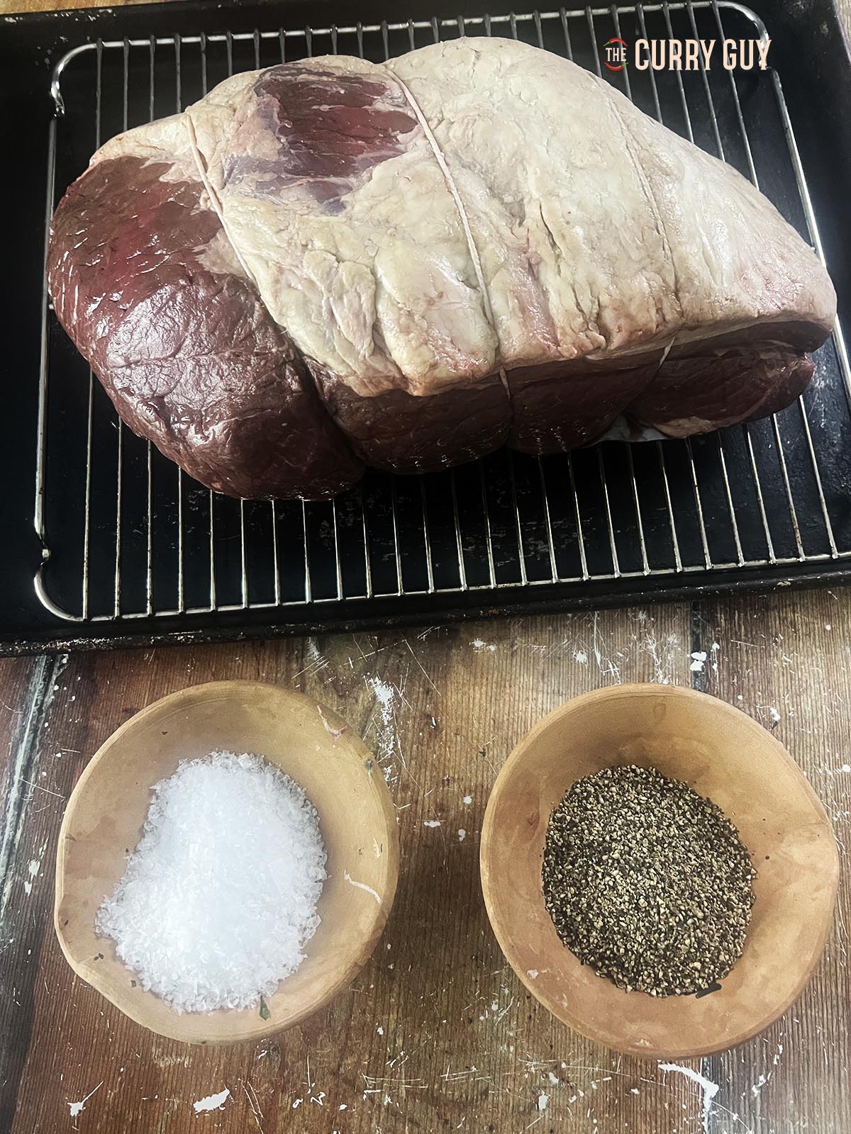The roast beef next to salt and pepper that will be applied to it.