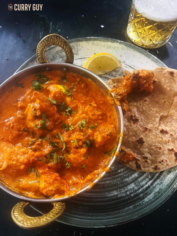 Chicken rezala served at the table with lemon wedges and paratha.