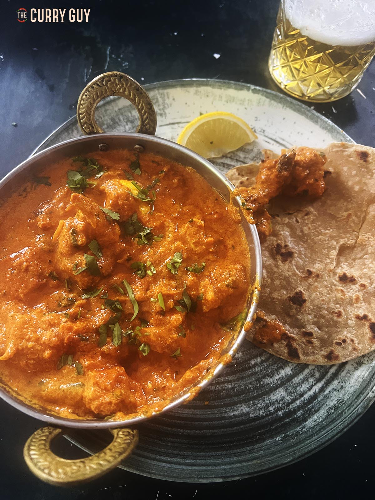 Chicken rezala served at the table with lemon wedges and paratha.
