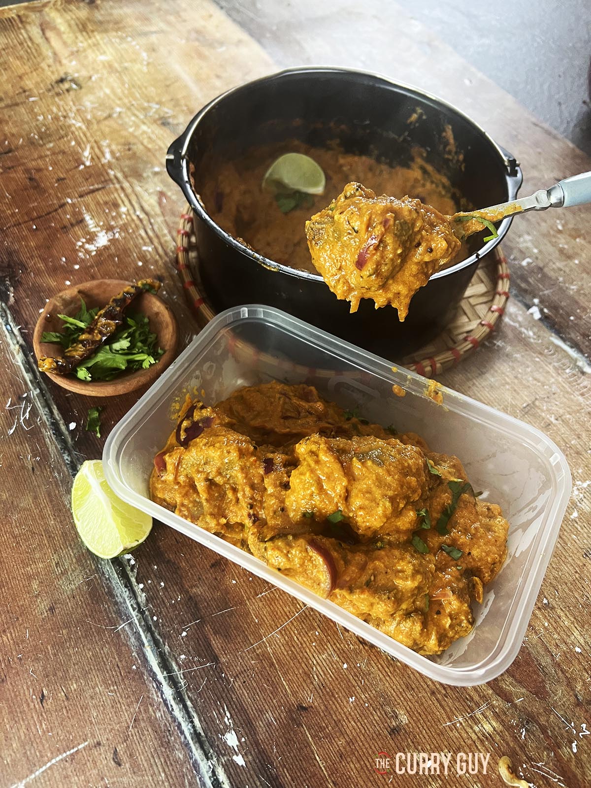 Lamb achari served in a takeaway container.