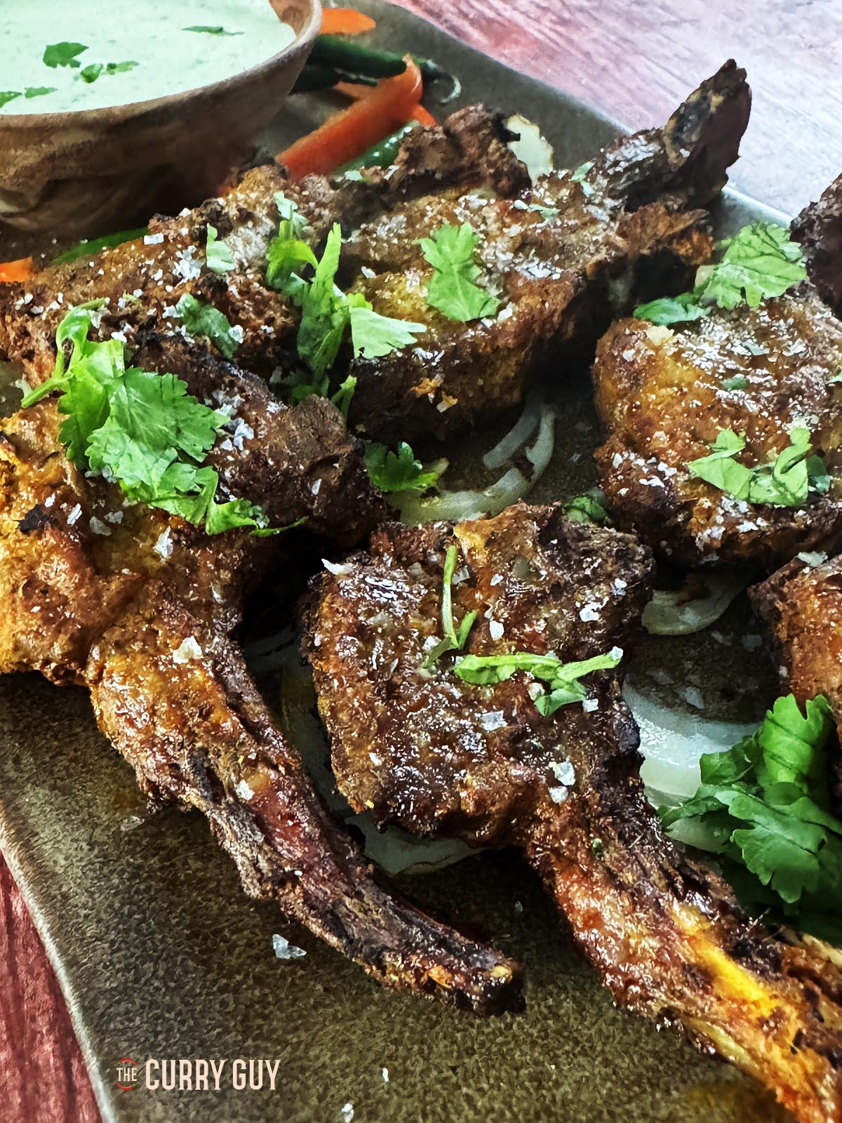 Air fryer lamb chops on a serving plate with raita and garnished with coriander. 