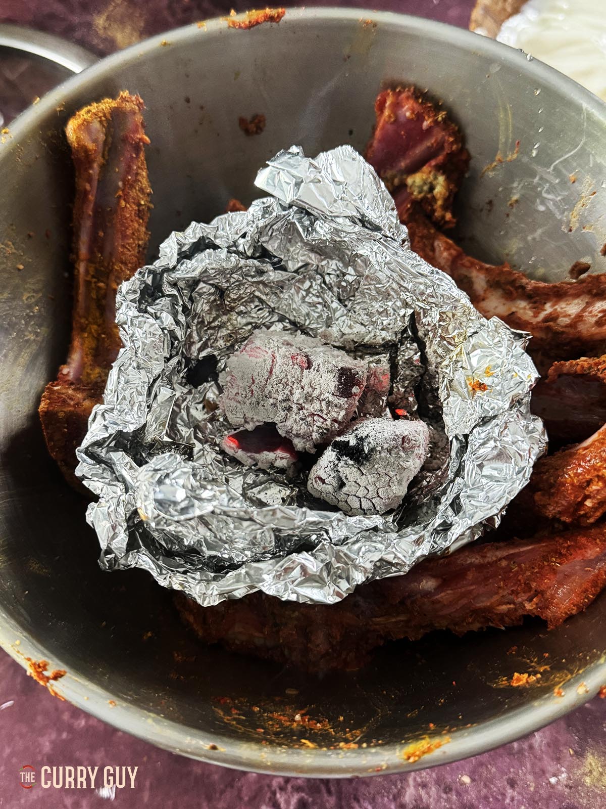 Burning charcoal on a piece of foil in the centre of the lamb chops in a mixing bowl.