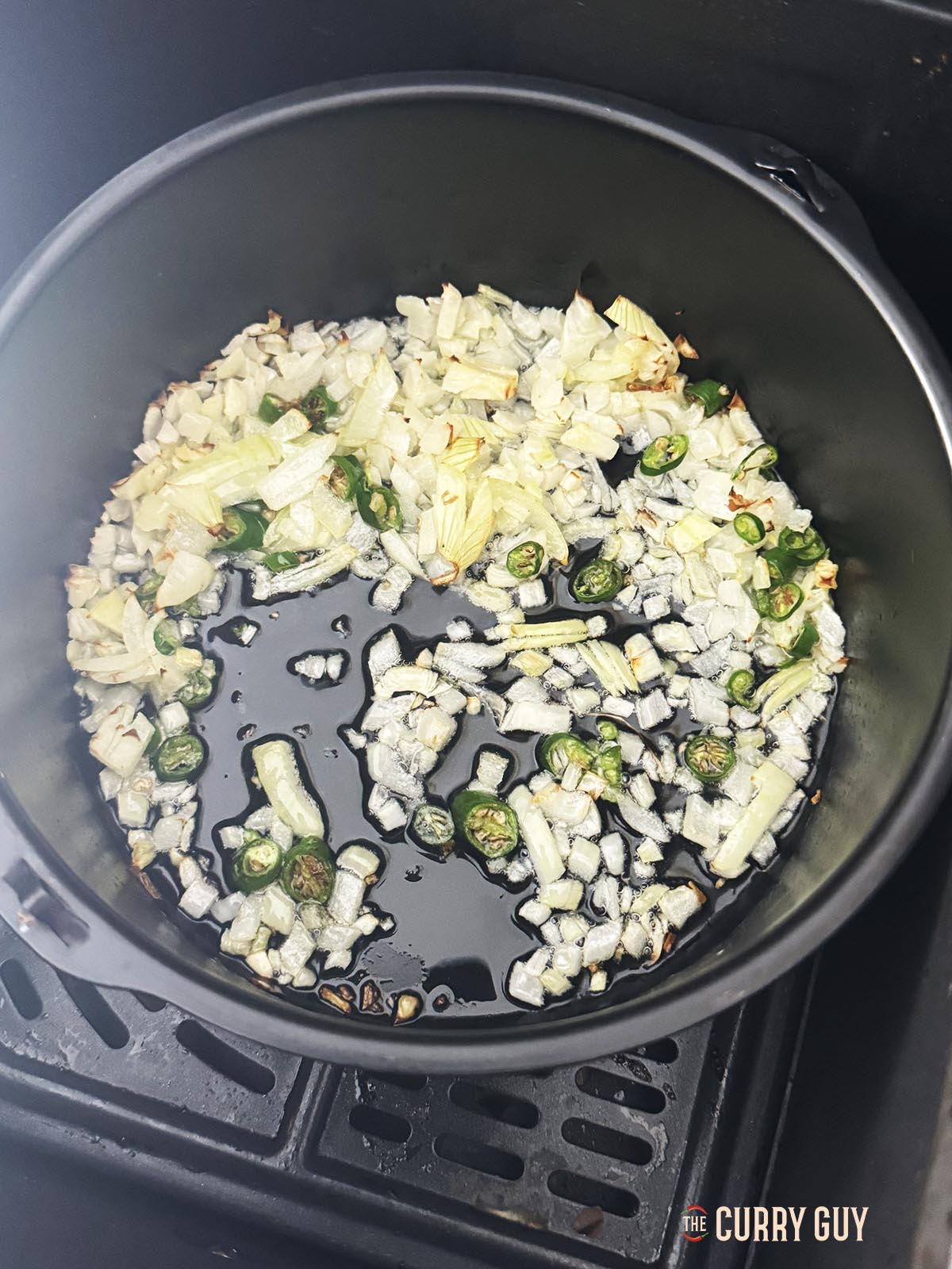 Frying chopped onions and chillies in oil in a cake tin in the air fryer.