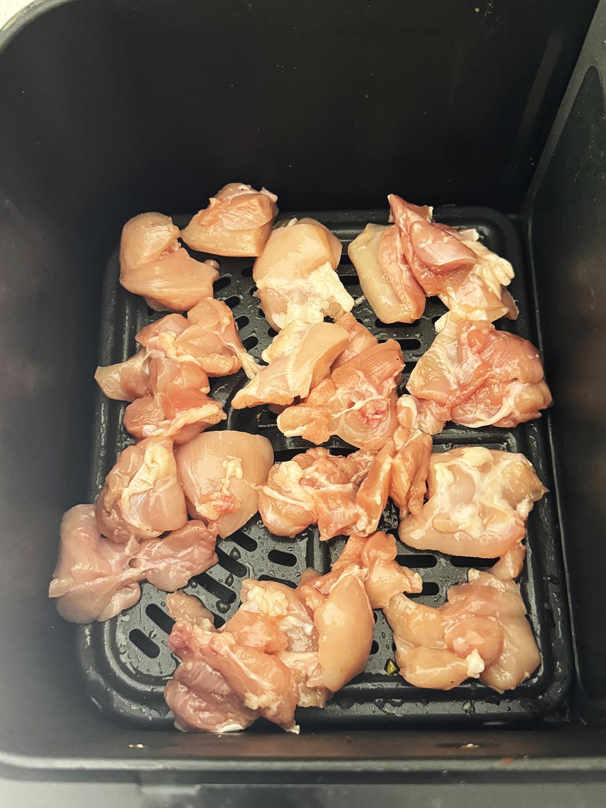 Raw chicken in the air fryer basket to cook.