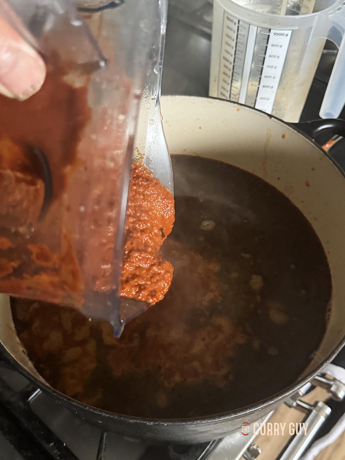 Pouring the blended chili paste into the broth in a large sauce pan.