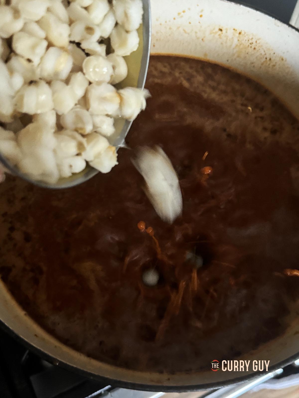Pouring the hominy into the simmering broth.