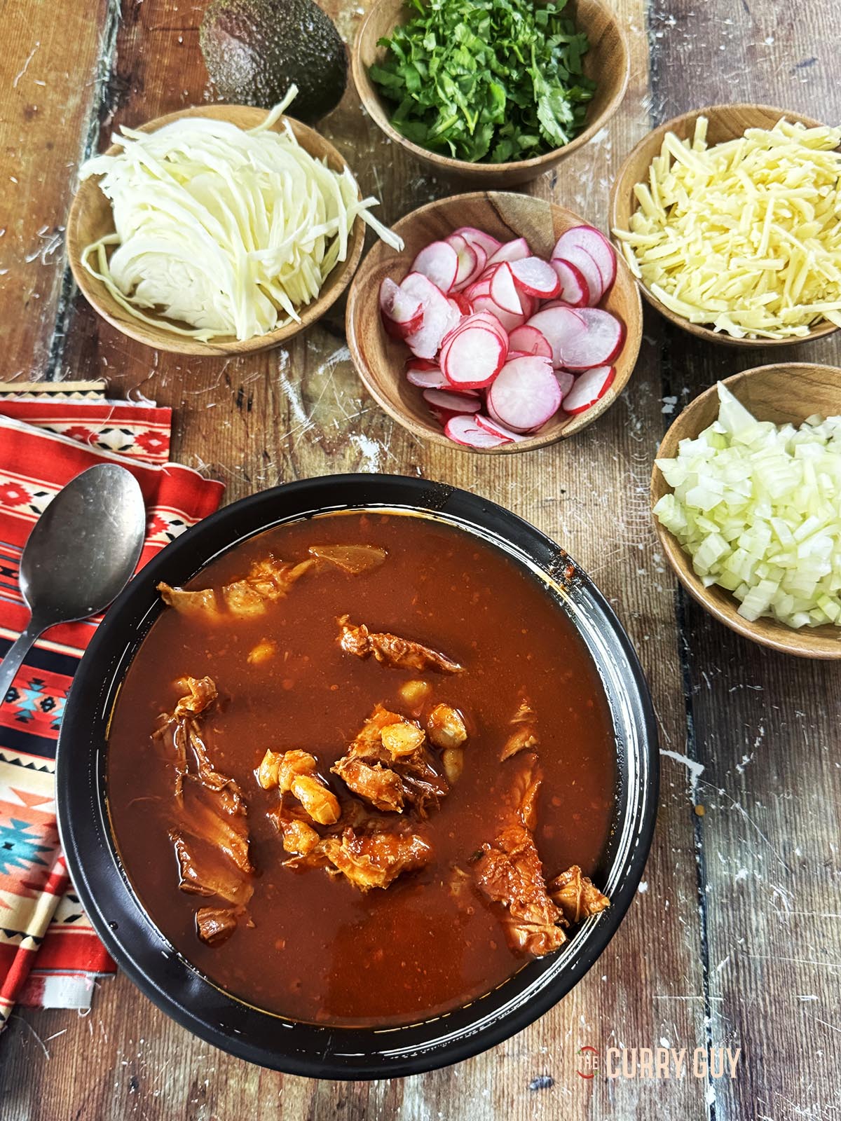 Dividing the pozole rojo into individual bowls and serving with a selection of garnishes.