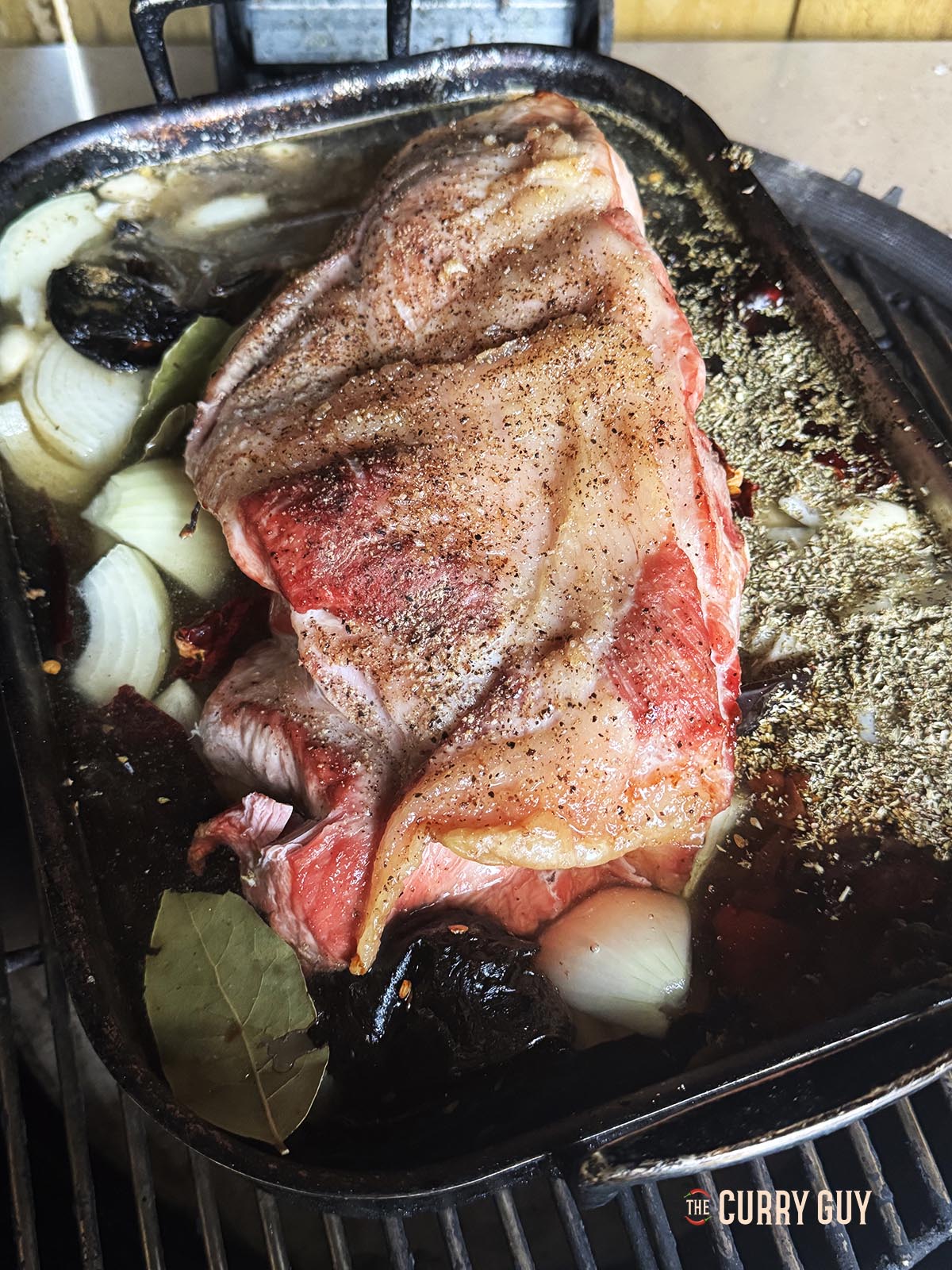 The pork shoulder in a casserole dish covered with water and the remaining ingredients.