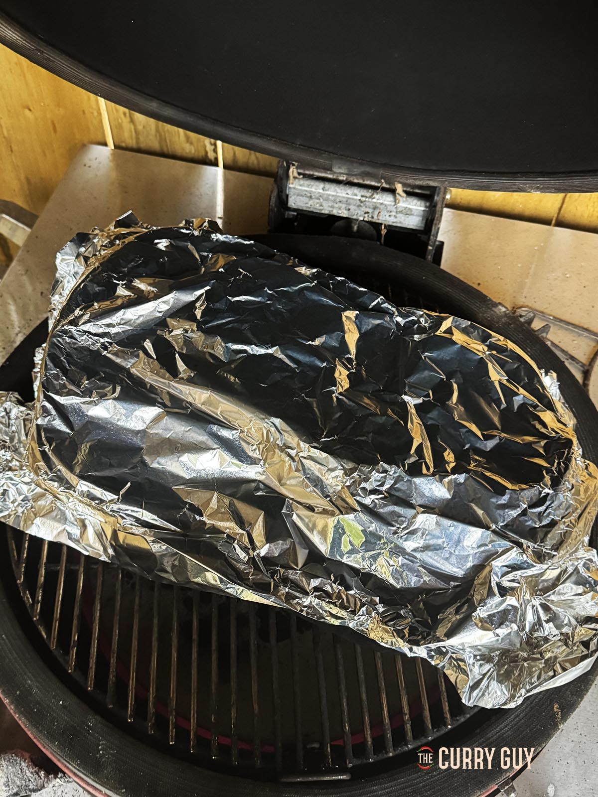 The pork covered with foil in a dish on the barbecue.