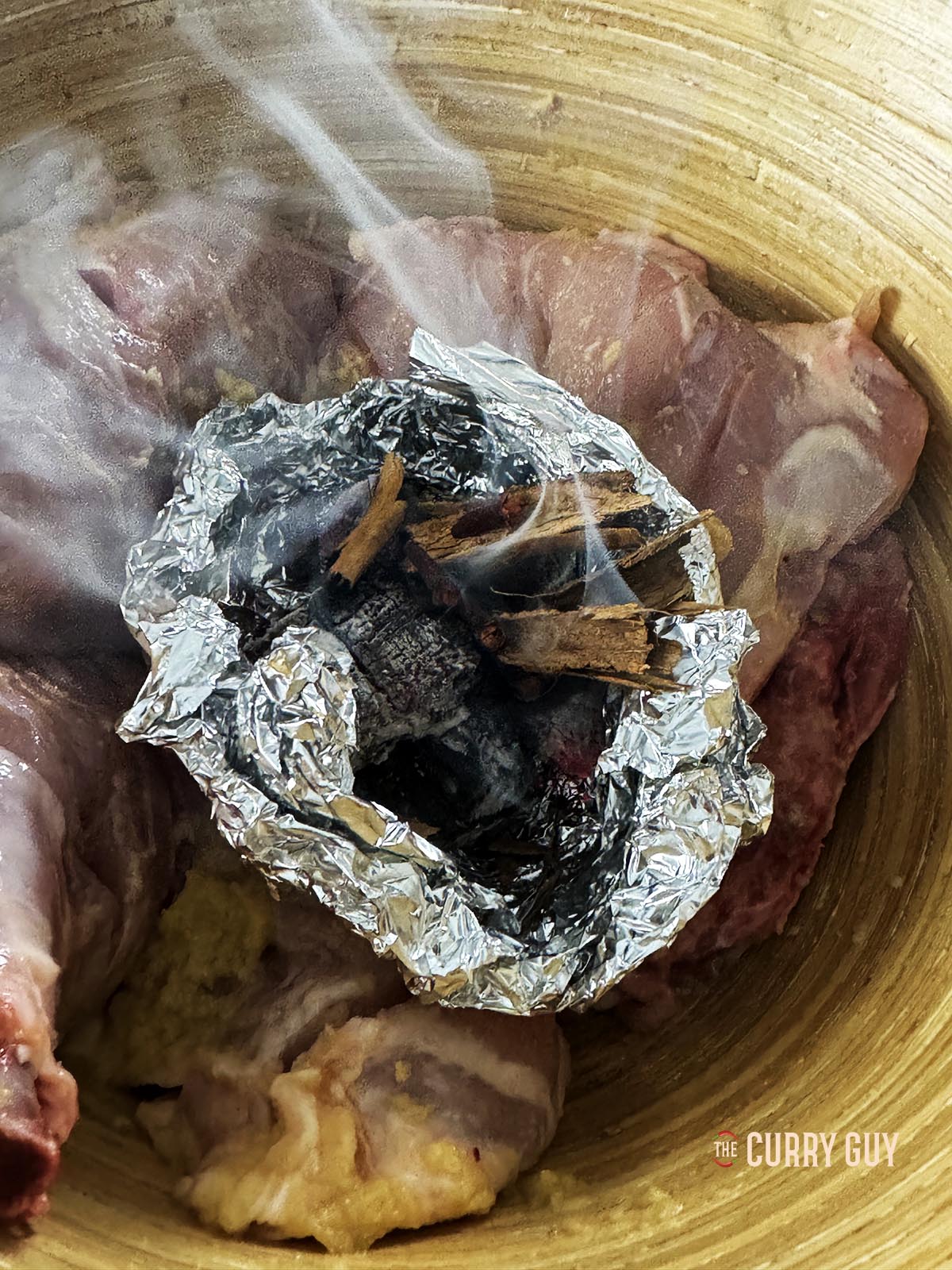 Charcoal burning with spices on a piece of foil sitting in the mixing bowl with the chicken.