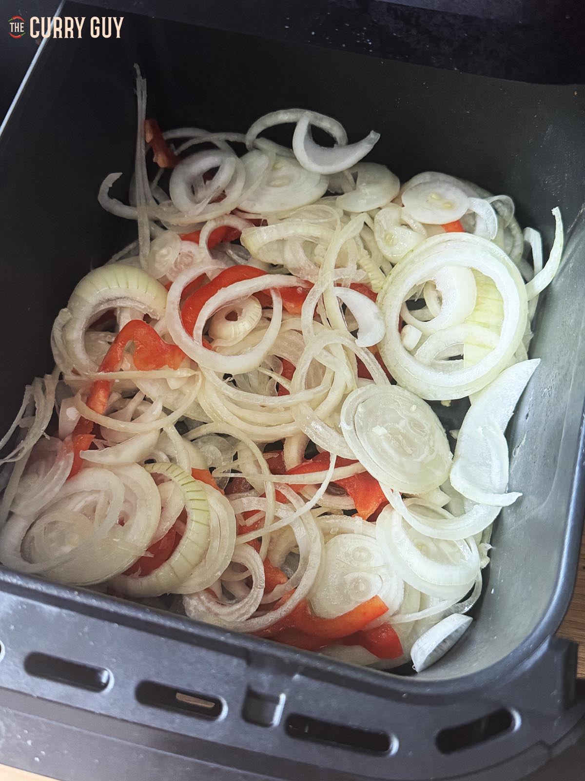 Placing the sliced onions and bell pepper in the air fryer basket to cook.