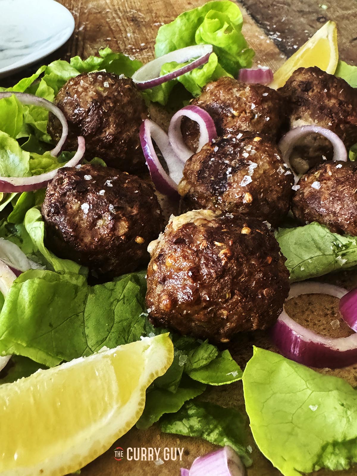 The koftas plated on a bed of lettuce, with lemons and sliced red onions.