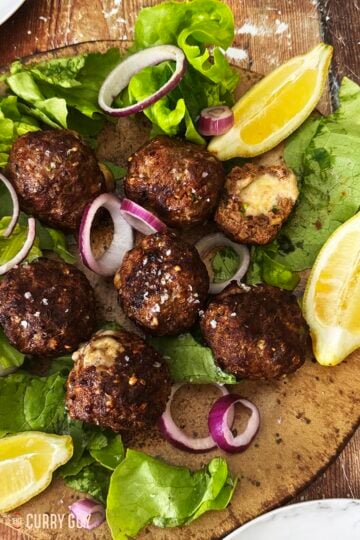 Cheese stuffed meatballs on a serving platter with lettuce, onions and lemon wedges.