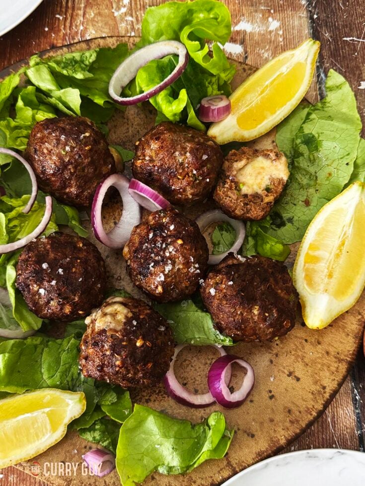 Cheese stuffed meatballs on a serving platter with lettuce, onions and lemon wedges.