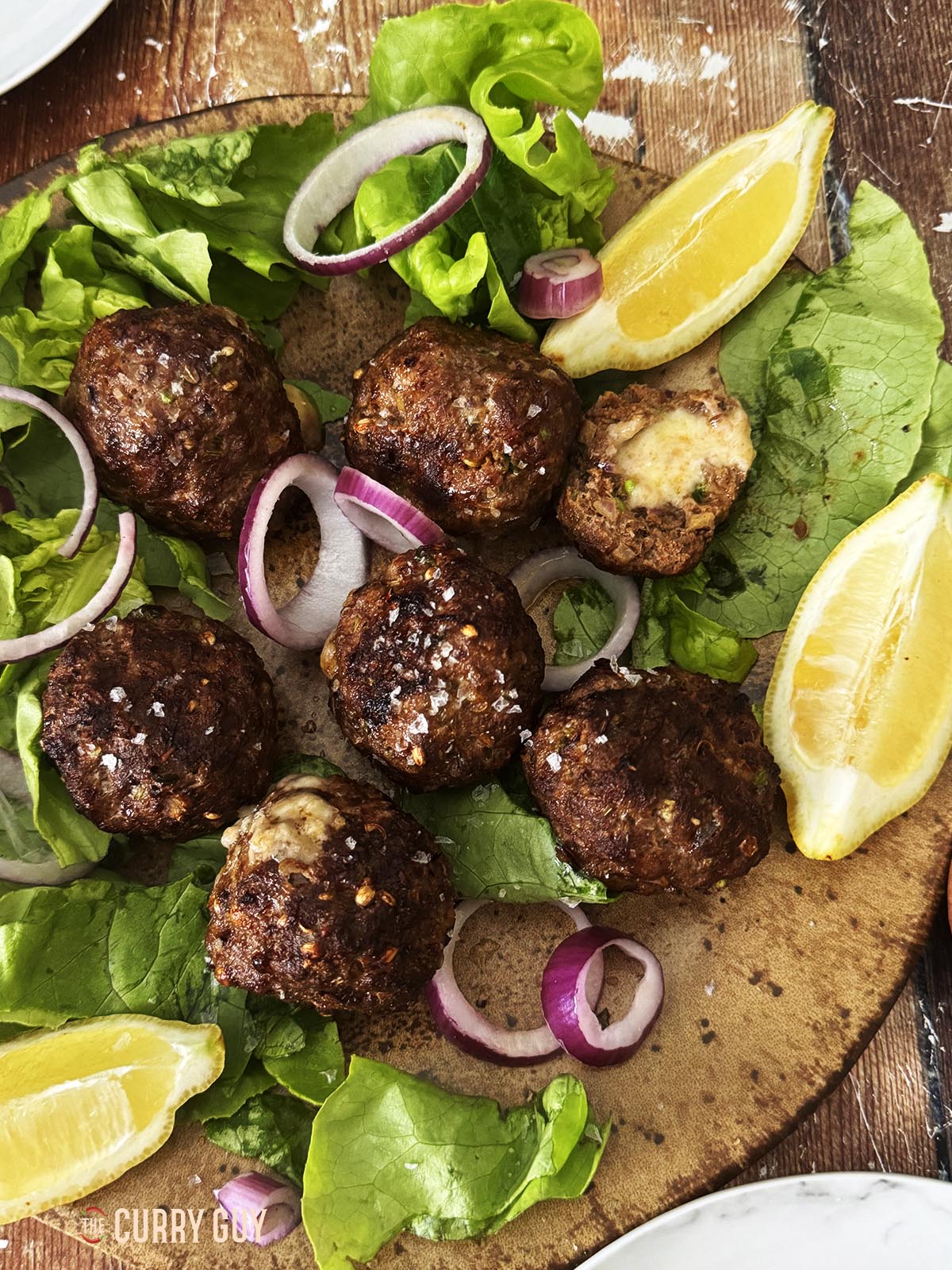Cheese stuffed meatballs on a serving platter with lettuce, onions and lemon wedges.