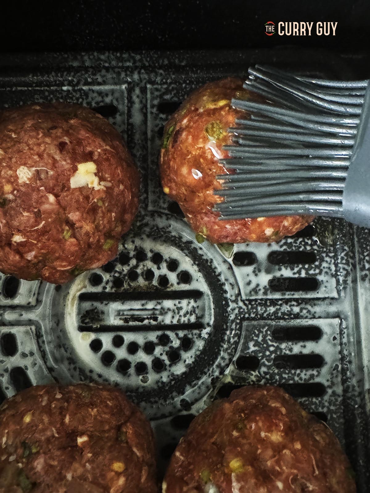Basting the koftas with ghee in the air fryer basket.
