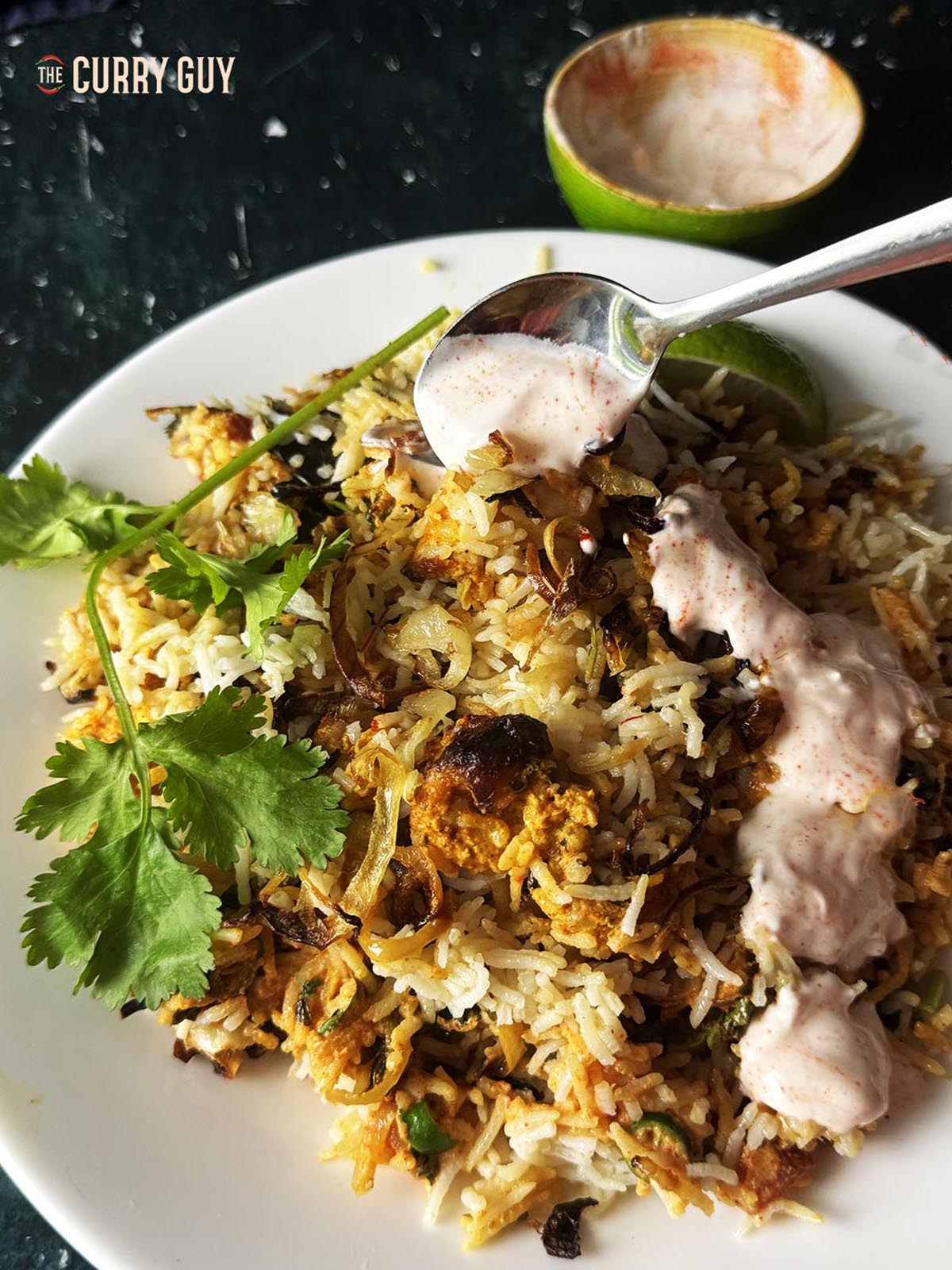 Air Fryer chicken biryani plated up and drizzled with chilli raita.