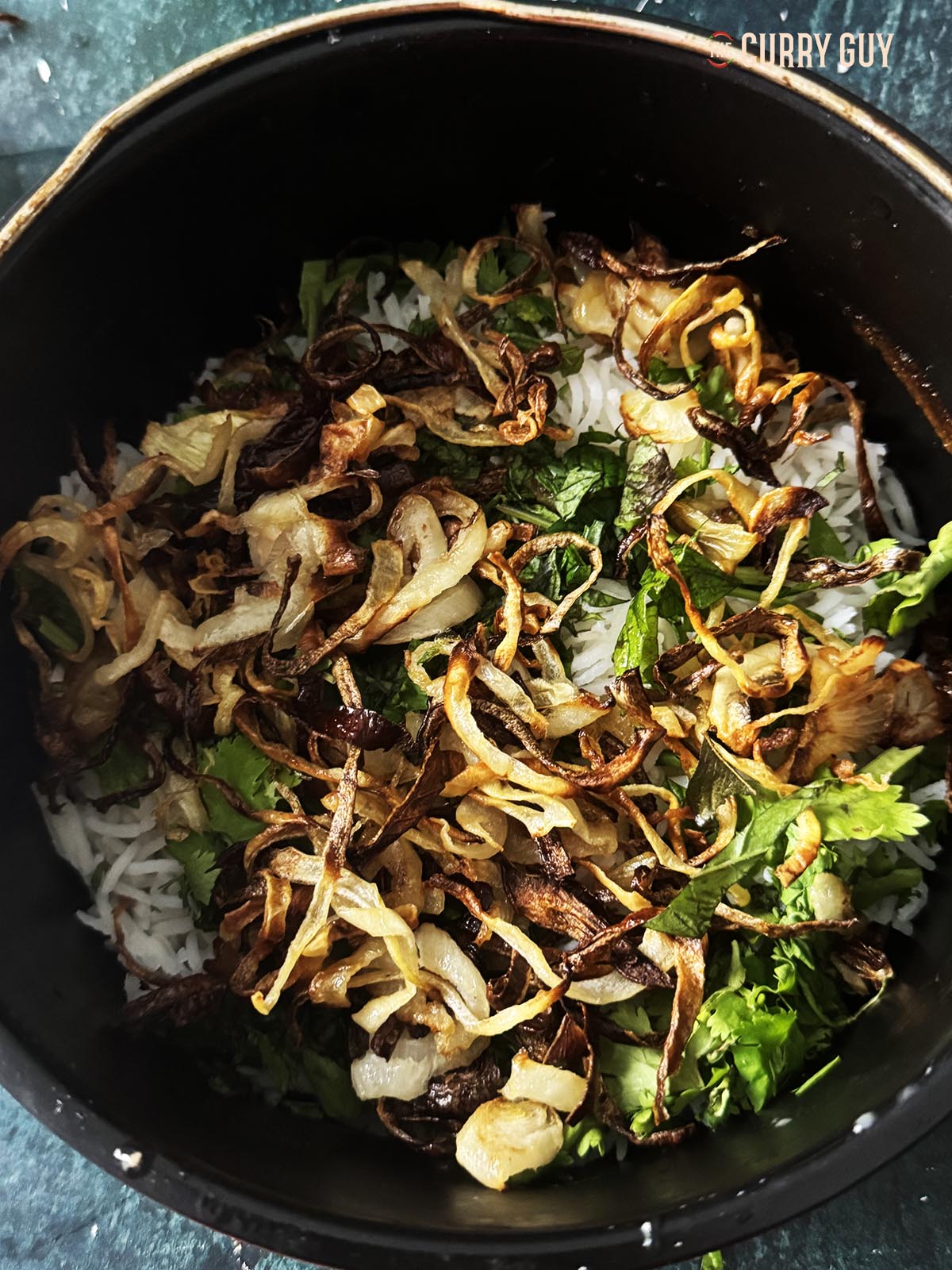 Adding half of the rice, fried onions, coriander and mint to the pan.